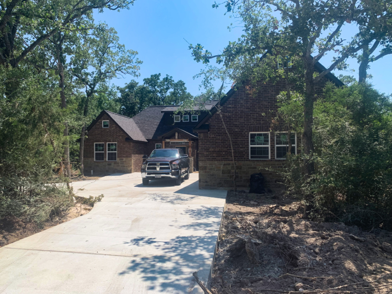 Front of new construction dark brick and stone house in woods with tall trees