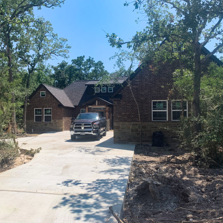 Front of new construction dark brick and stone house in woods with tall trees